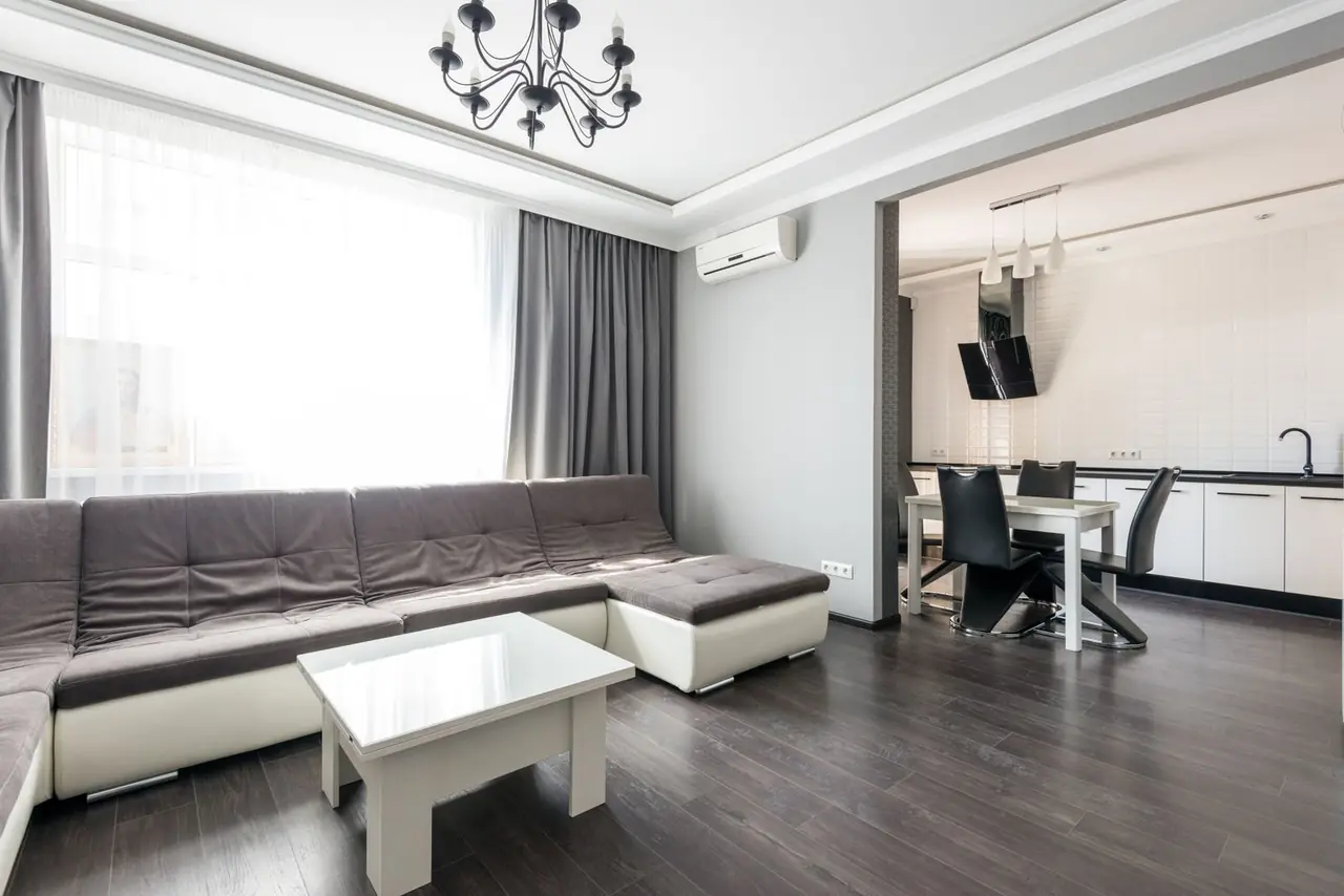 Interior of modern white flat furnished with comfortable couch and dining zone with wooden floor and white wal
